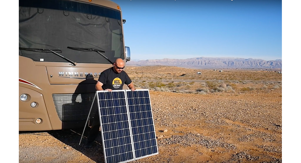 A man setting up portable solar panels in front of his Winnebago RV