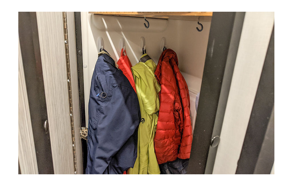 Hooks on the wall in the bathroom with snow pants and jackets hanging from them.