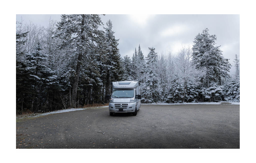 Winnebago Trend parked on pavement surrounded by snow covered trees