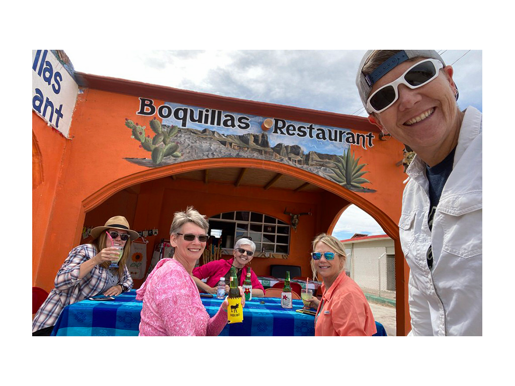 Noel taking a selfie with four friends in background sitting at table outside of Mexican restaurant