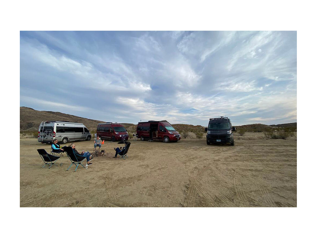 Four people sitting in camp chairs in a circle with four Travatos in background