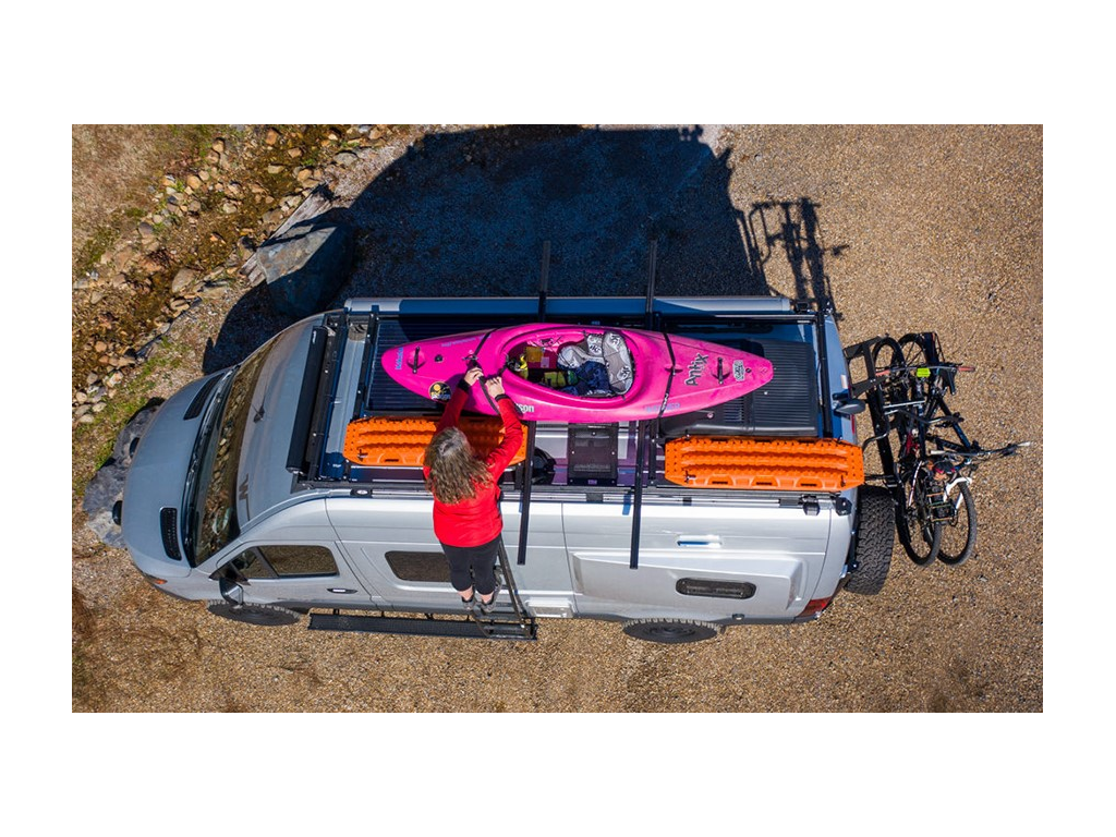 Kathy standing on Revel side ladder tying kayak to roof rack. Two Max Trax are attached to roof rack as well.