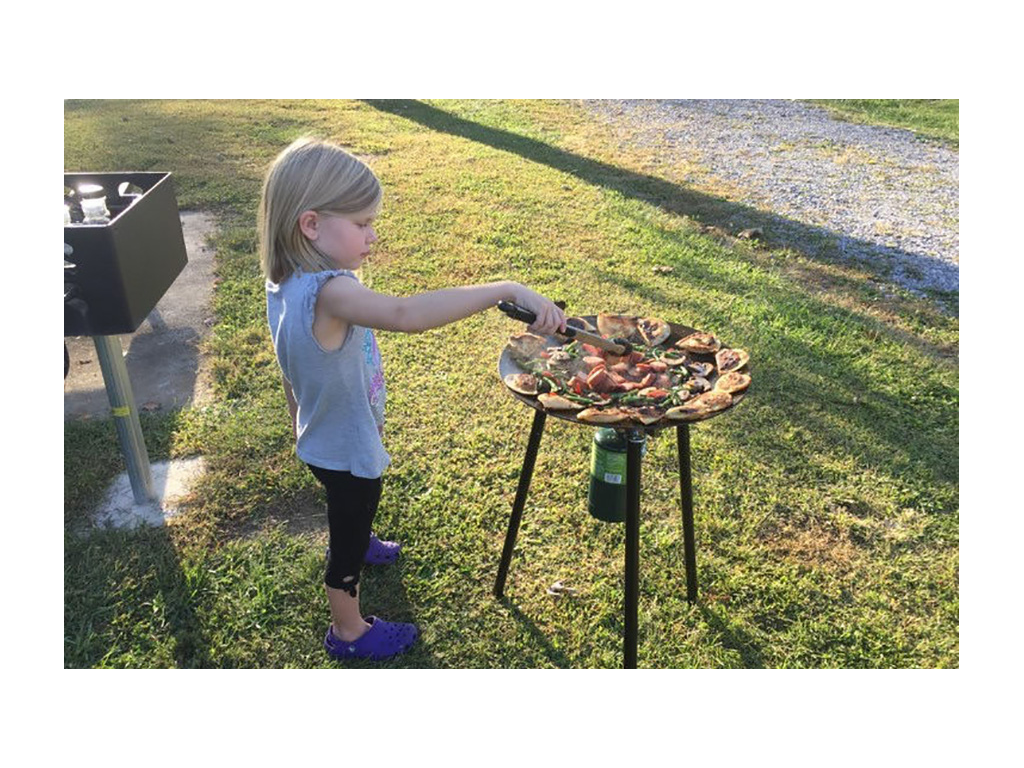 Young girl using tongs to flip food on skottle