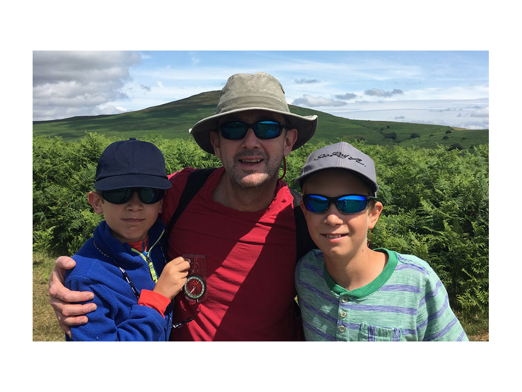 Huw Bower with kids smiling in front of green rolling hills