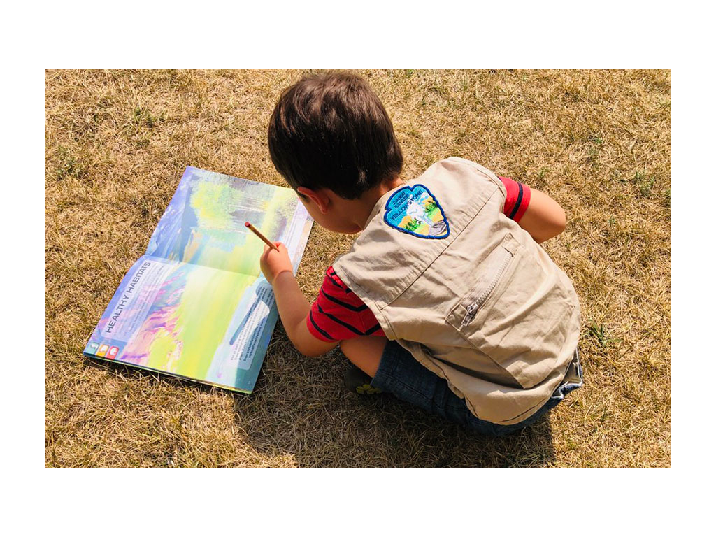 Caspian sitting on grass writing in the junior ranger booklet