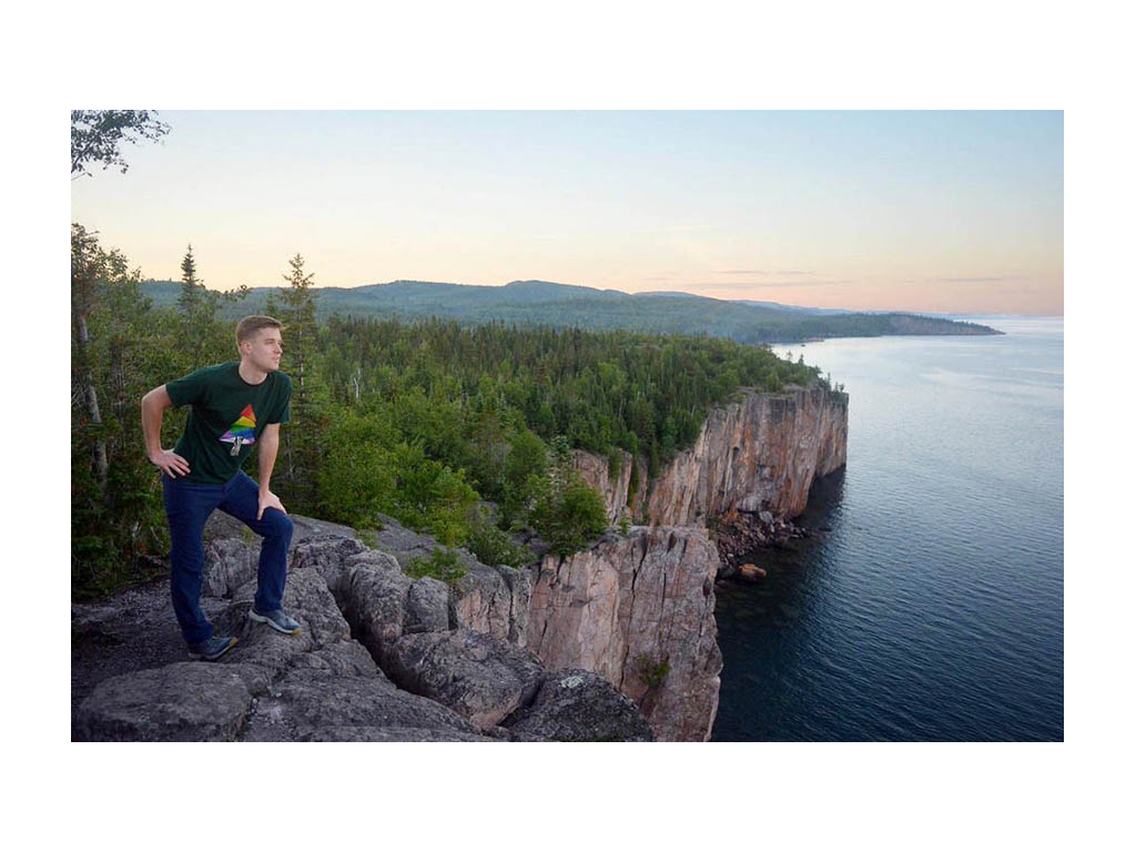 Mikah standing on bluff wearing black shirt with Safe Space logo on it