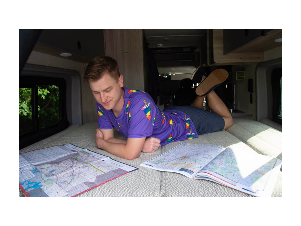 Mikah laying on bed planning route with two paper maps