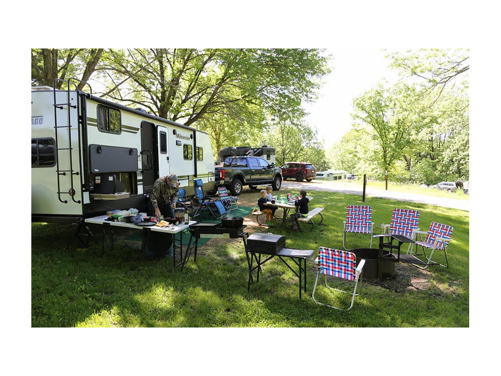 Children sitting at picnic table and food set up on fold up table outside of travel trailer