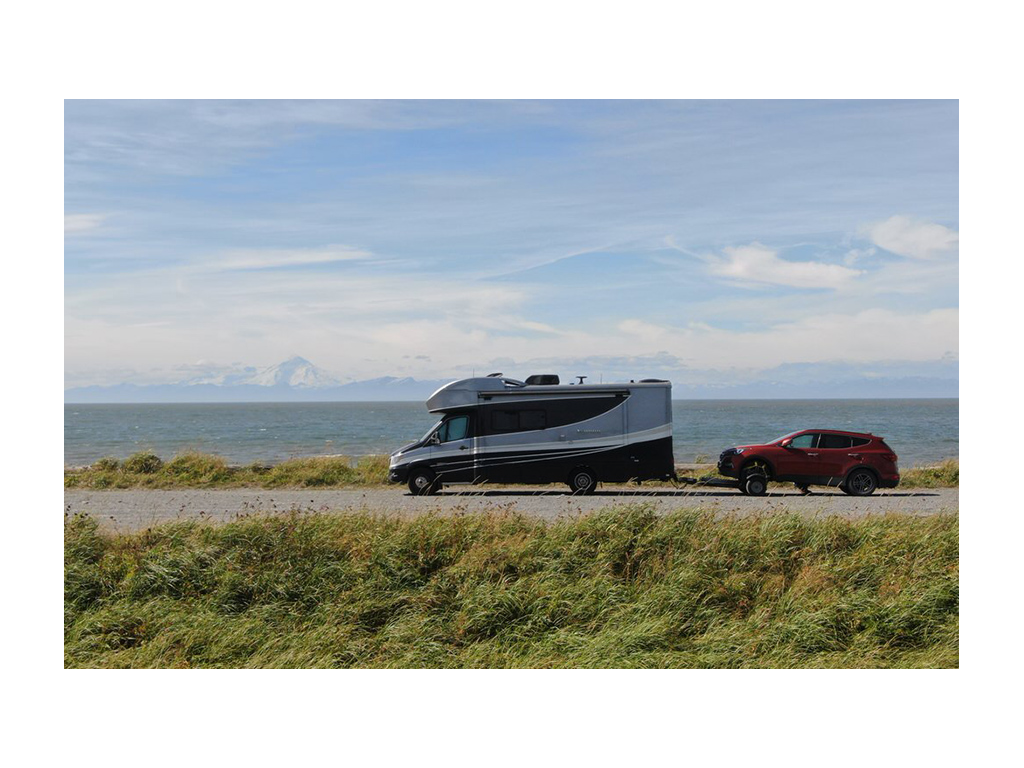 Navion pulling tow car down road along water