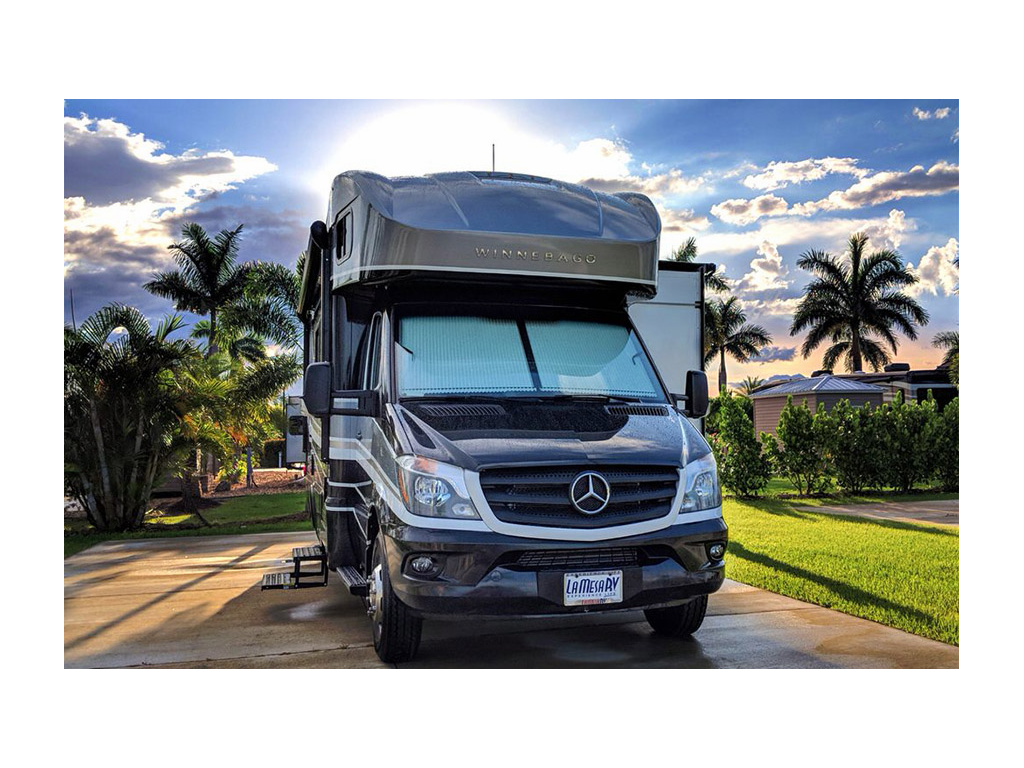 Navion parked on concrete at campground with palm trees in background