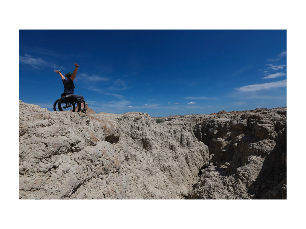 Nerissa at No Barriers with arms thrown up in air on top of a mountain