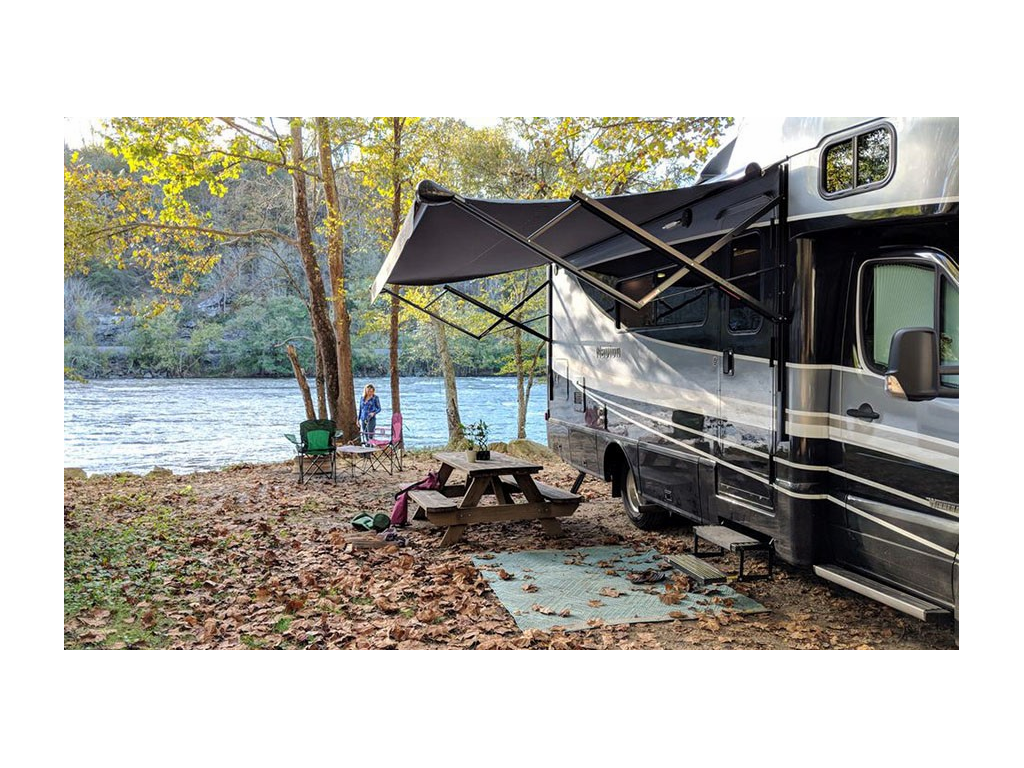 Navion parked at campsite near water with awning extended