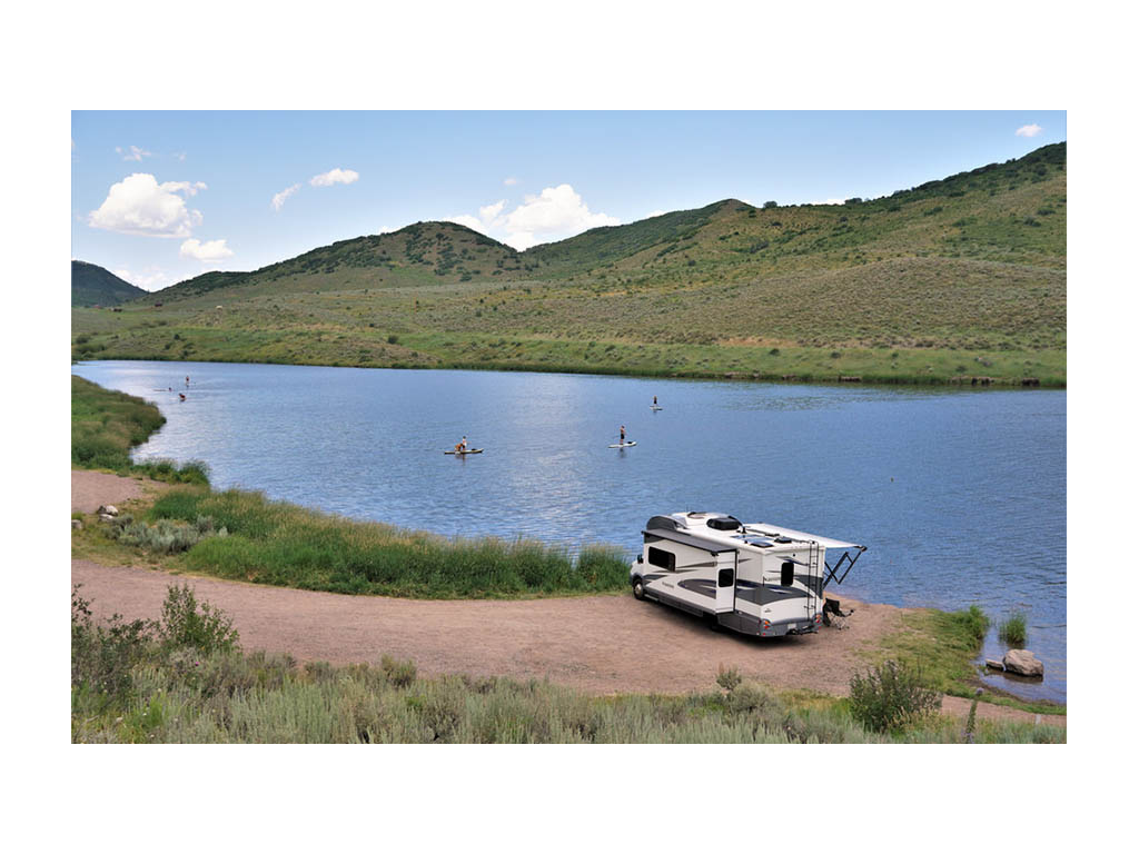 Navion parked in front of Stagecoach Reservoir. People are paddle boarding and kayaking on water