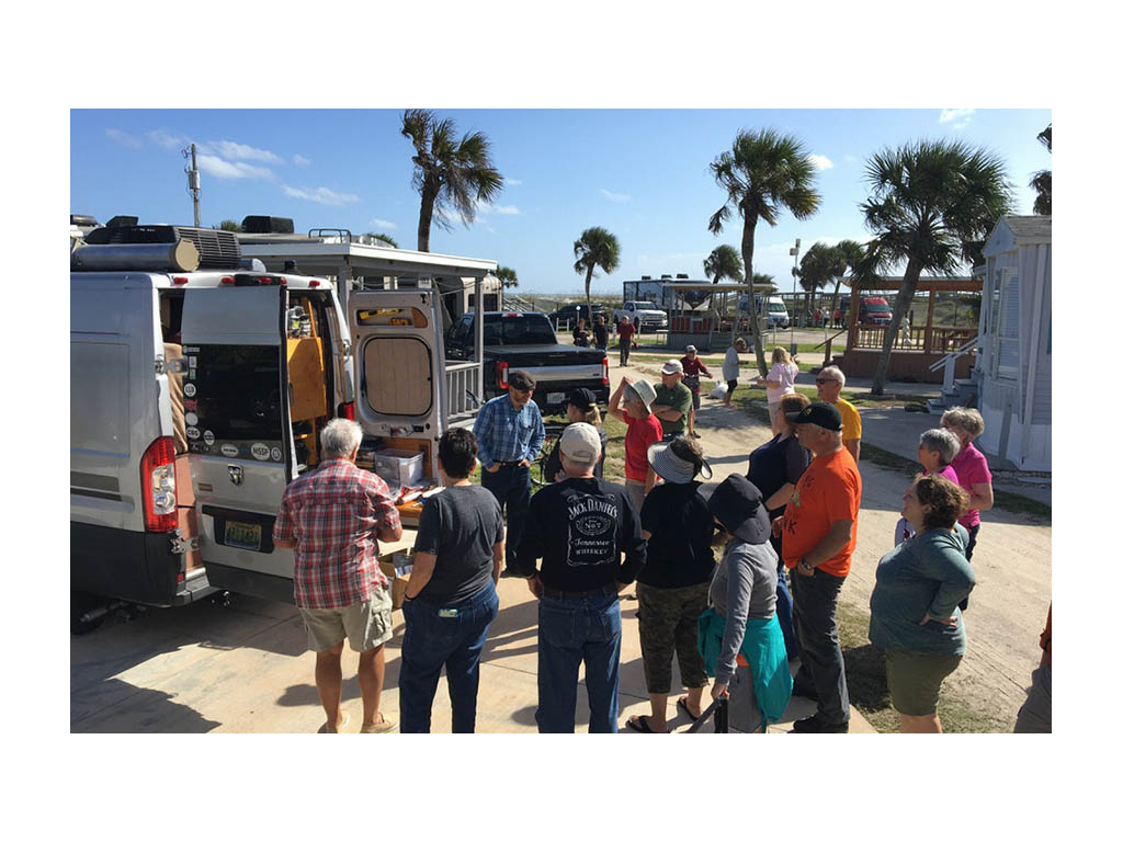 Scott teaching lesson to RV group standing in circle around silver Travato.