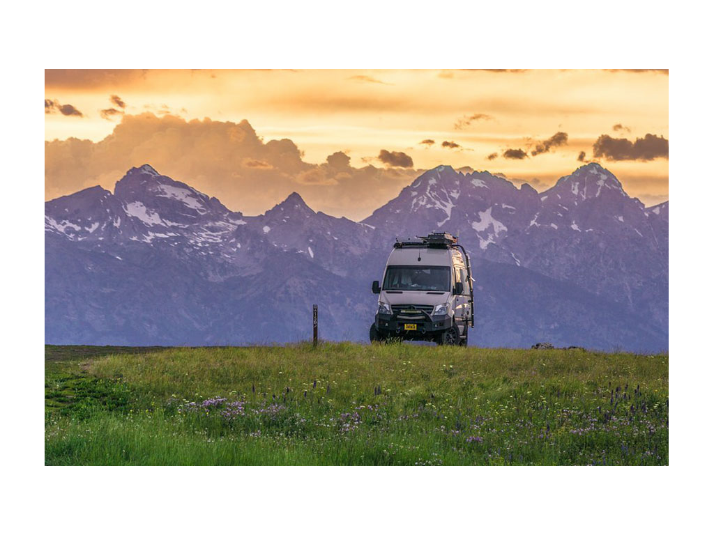 Winnebago Revel (Gnar Wagon) parked in grass with mountains and colorful sunset in background