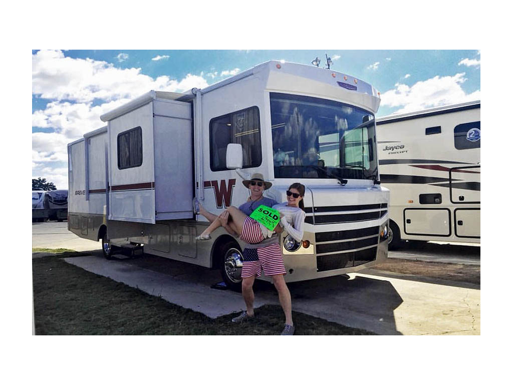 Heath holding Alyssa in front of Winnebago Brave with a bright green sold sign