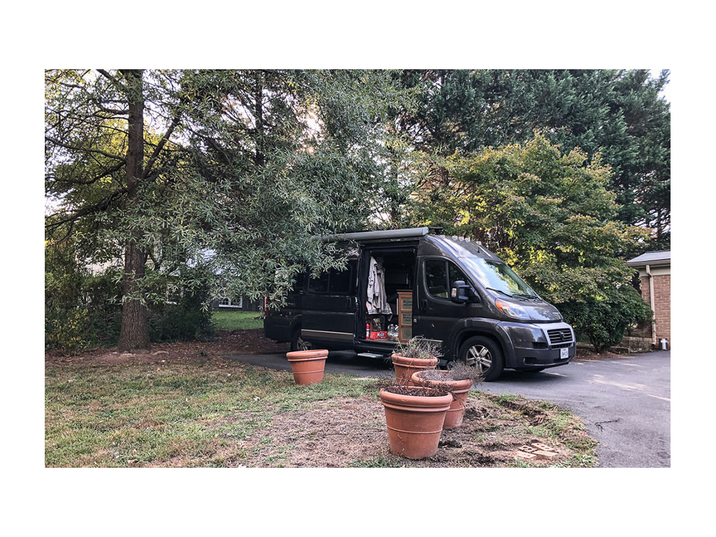 Travato parked near house under large trees