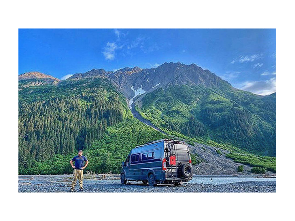Nick Riebe standing next to Travato with green mountains in the background
