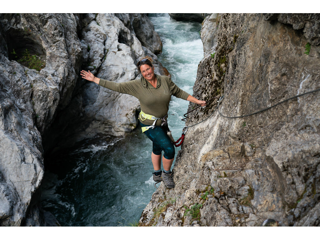 Kathy leaning back on a climb down a cliff side with a river below her