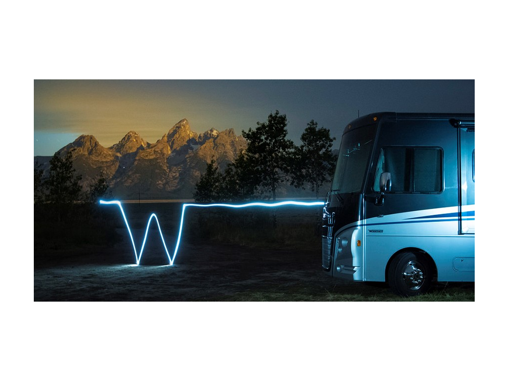 Lit Flying W and Winnebago Adventurer with mountains and trees in background