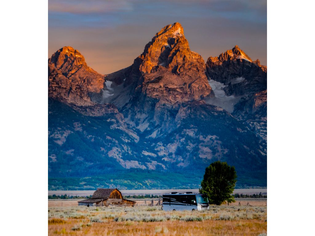 Adventurer parked in field with a barn and the Teton Mountain Range in the background