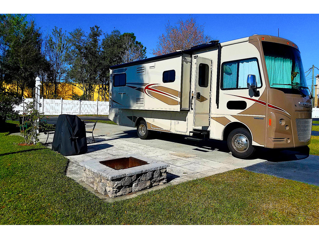 WInnebago Vista parked at KOA in Florida with nice paved patio outside with fire pit and grill