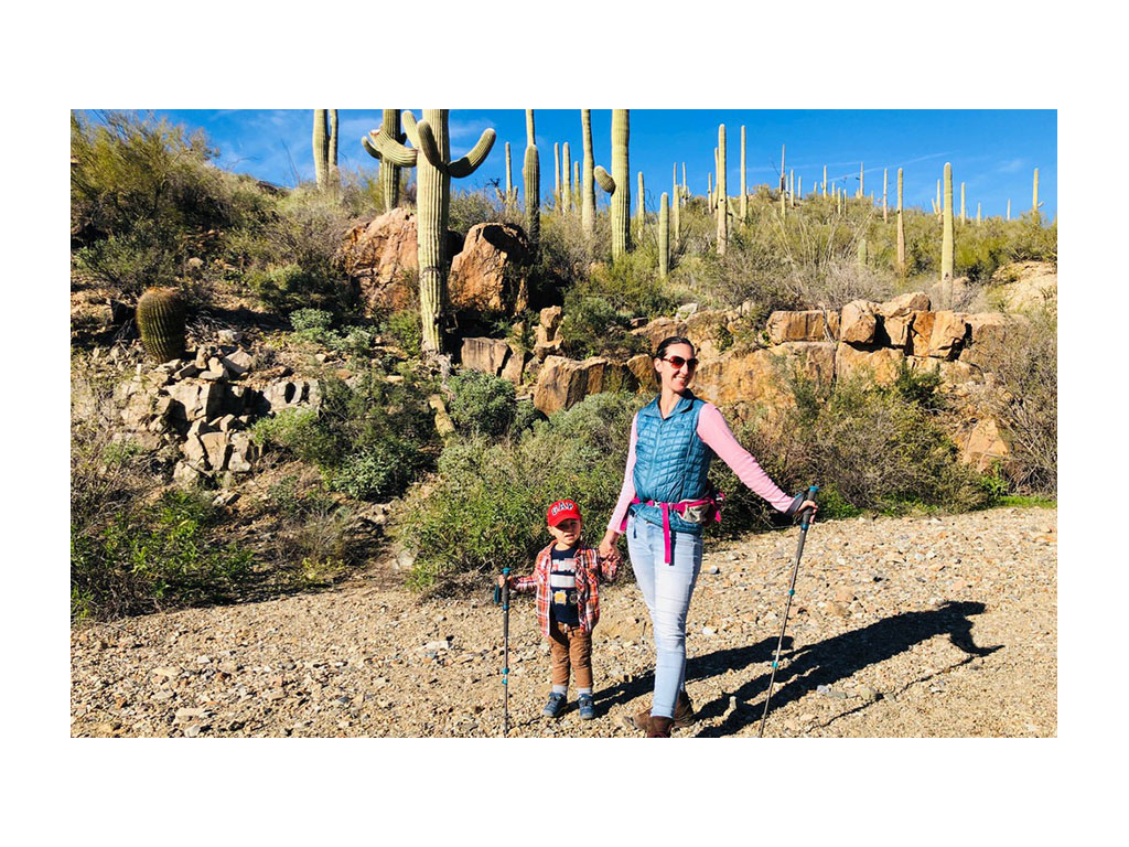 Brittany and Caspian hiking holding hiking sticks with many cacti in the background