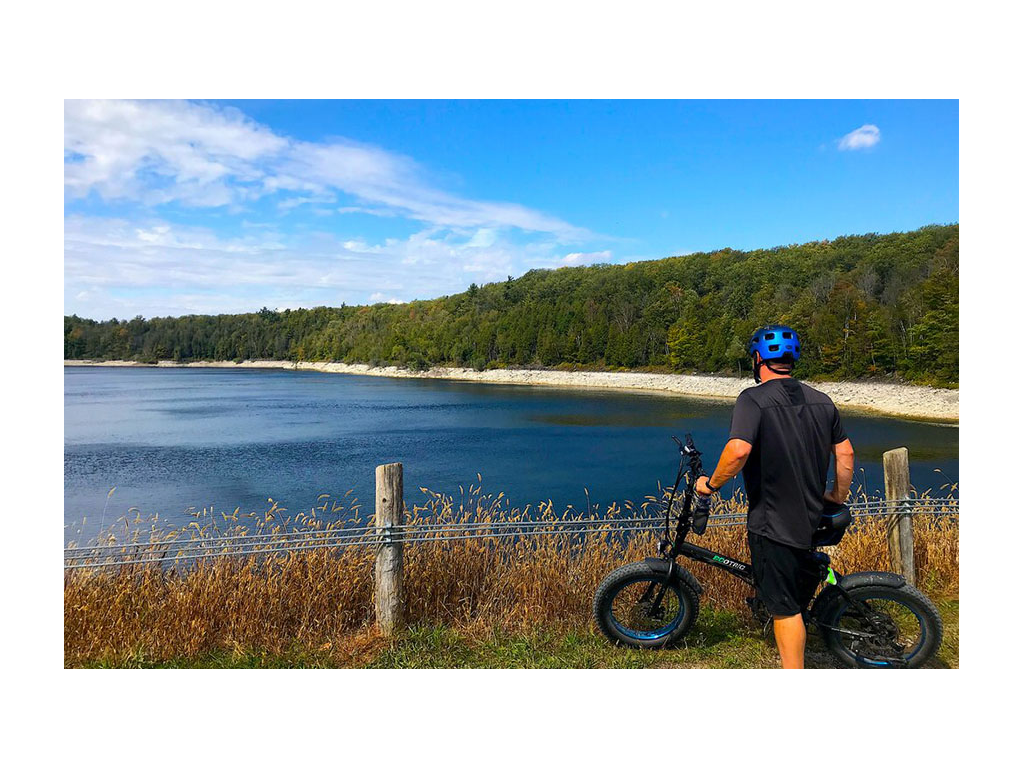 Kenny standing next to bike looking towards lake surrounded by trees