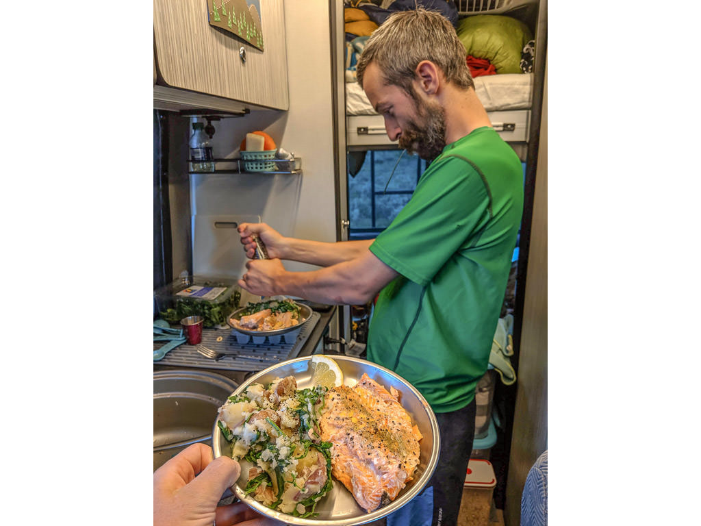 David grinding pepper on a plate full of food. Kelly's hand is in picture holding a silver plate with grilled salmon and a side