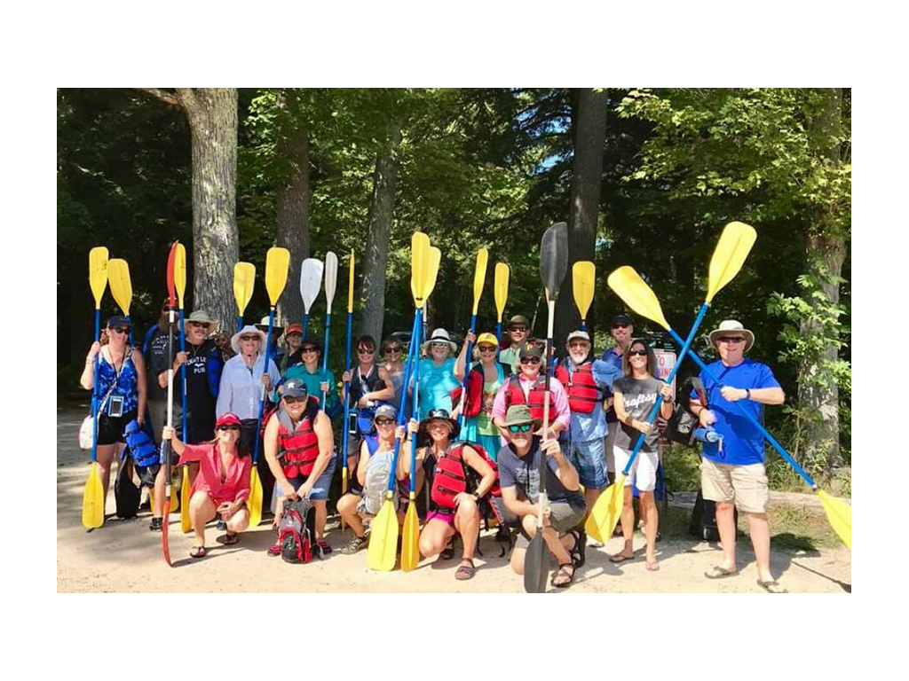 Large group of people holding up kayak paddles