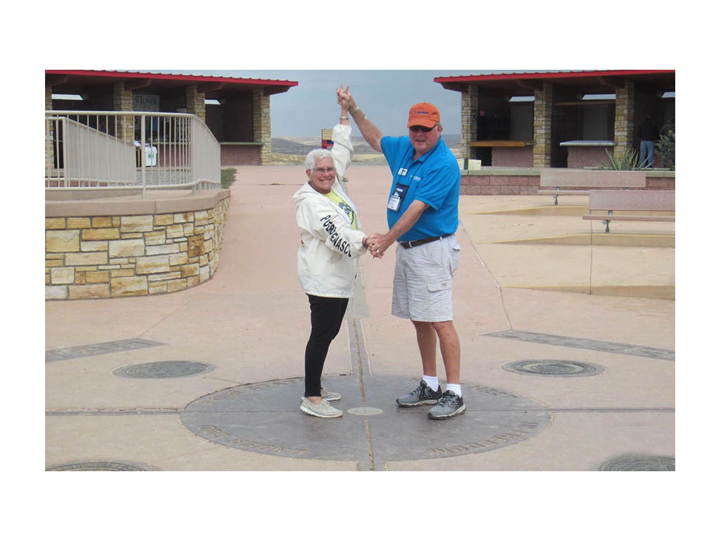 Jeanie and Andy standing on Four Corners sign holding hands.