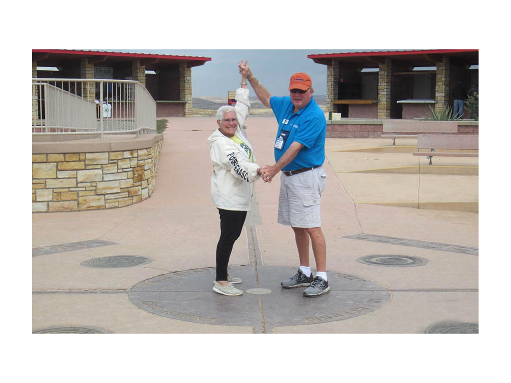 Jeanie and Andy standing on Four Corners sign holding hands. 