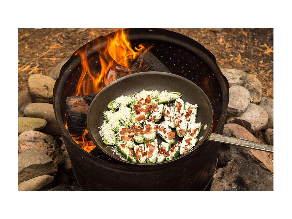Jalapeno poppers in a pan roasting over a campfire