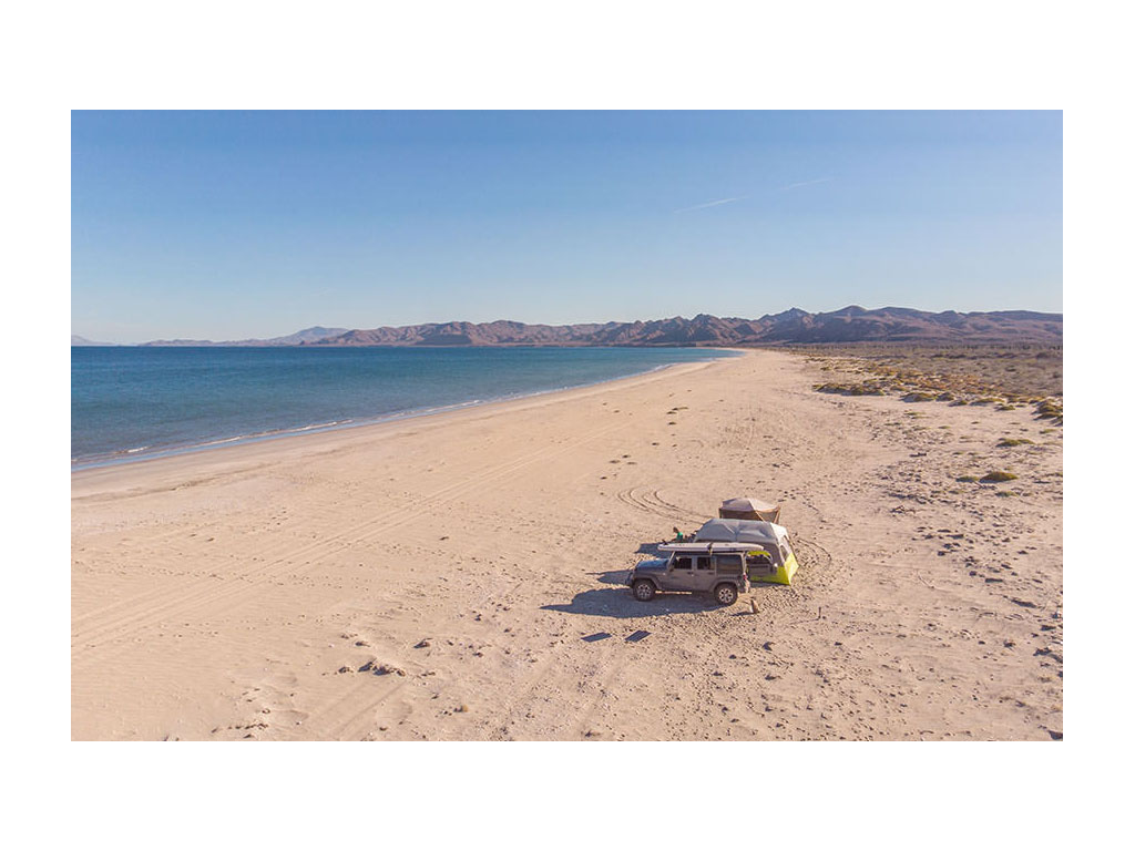 Jeep parked on beach next to two tents