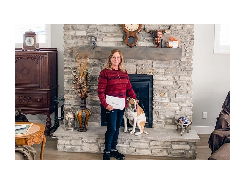 Family member holding stack of mail - standing next to white and tan dog in front of fireplace