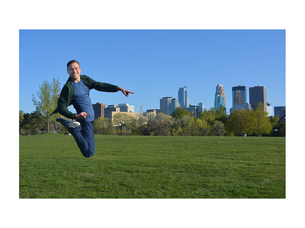 Mikah jumping in air pointing to buildings in City Park