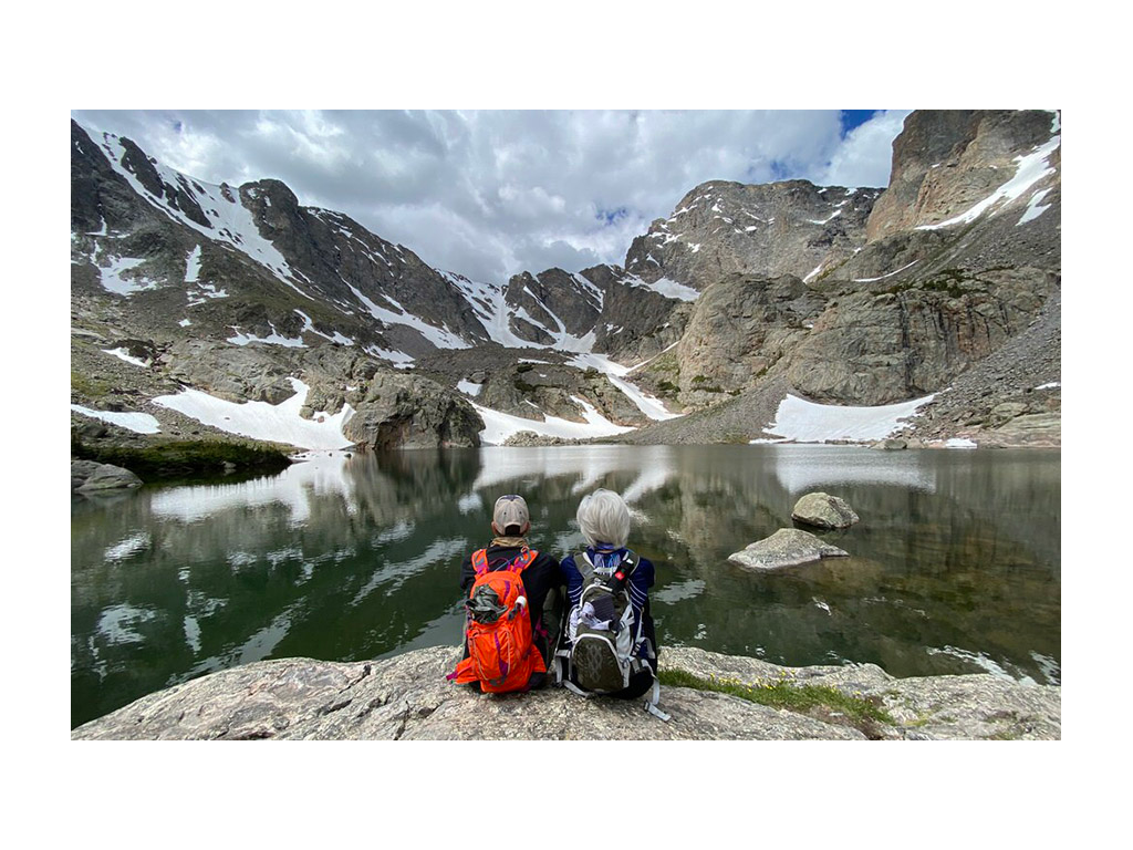 Noel and Chris sitting on a rock next to water looking at mountains