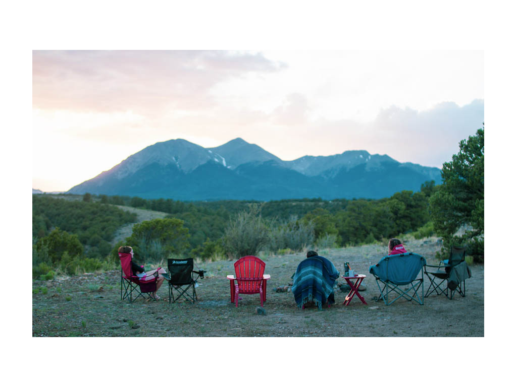 Shot from behind of three friends sitting in camp chairs looking at mountain view