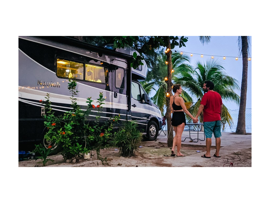 The Newstate Nomads holding hands next to Navion parked on beach