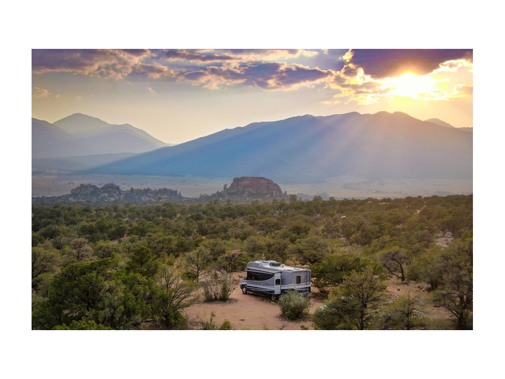 Navion boondocking in large open field. Sun is setting over mountains