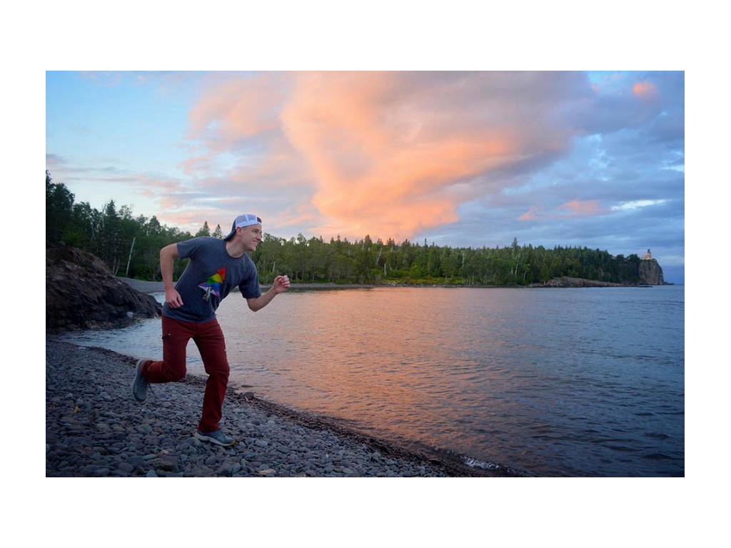 Mikah pretending to run next to water with colorful sky in background.