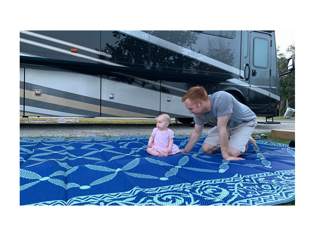 Heath and Ellie sitting on outdoor rug outside of RV