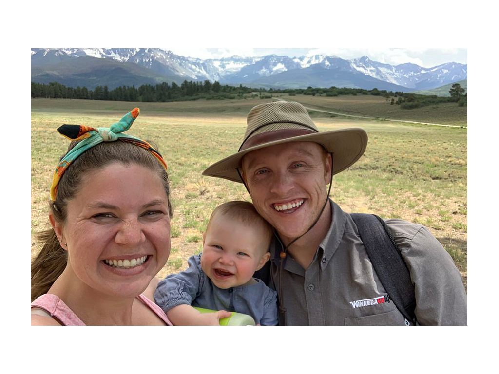 Alyssa, Elli and Heath smiling for a selfie. Mountains are in the distance behind them.
