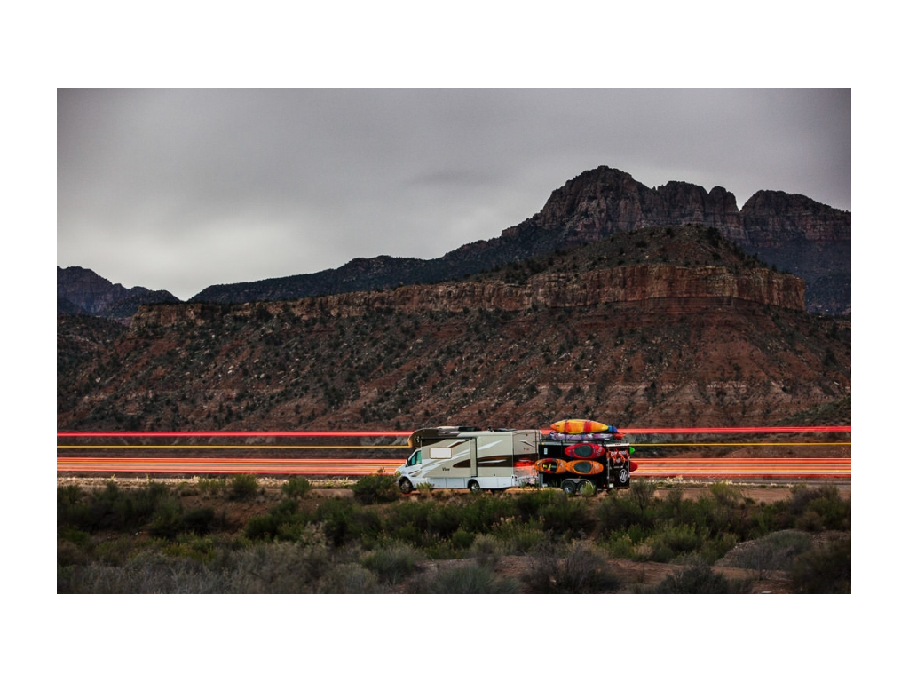 View driving in front of mountains pulling trailer with many kayaks