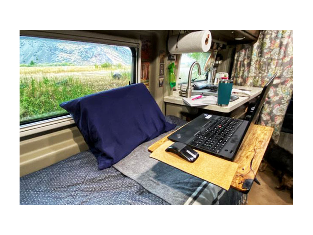 Wooden desk with laptop on it over Travato bed