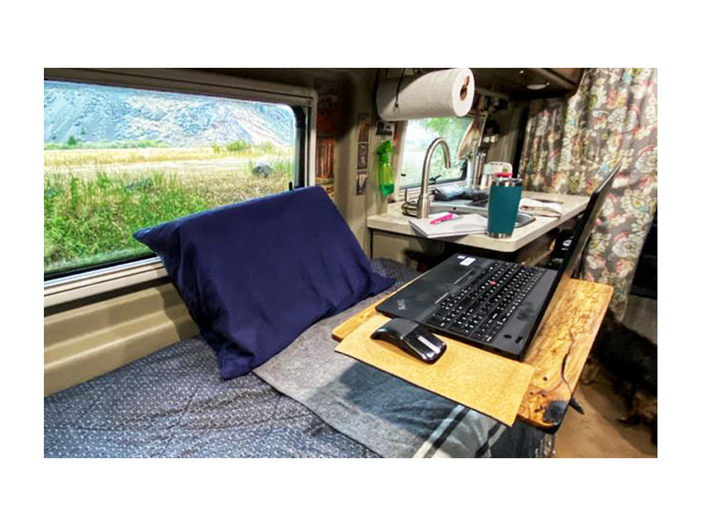 Wooden desk with laptop on it over Travato bed 
