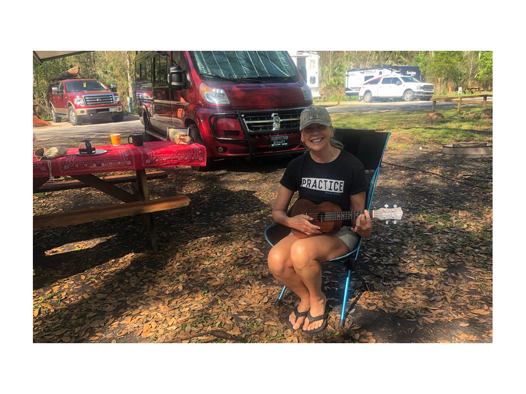 Viki playing ukulele in camp chair next to Travato at campground.