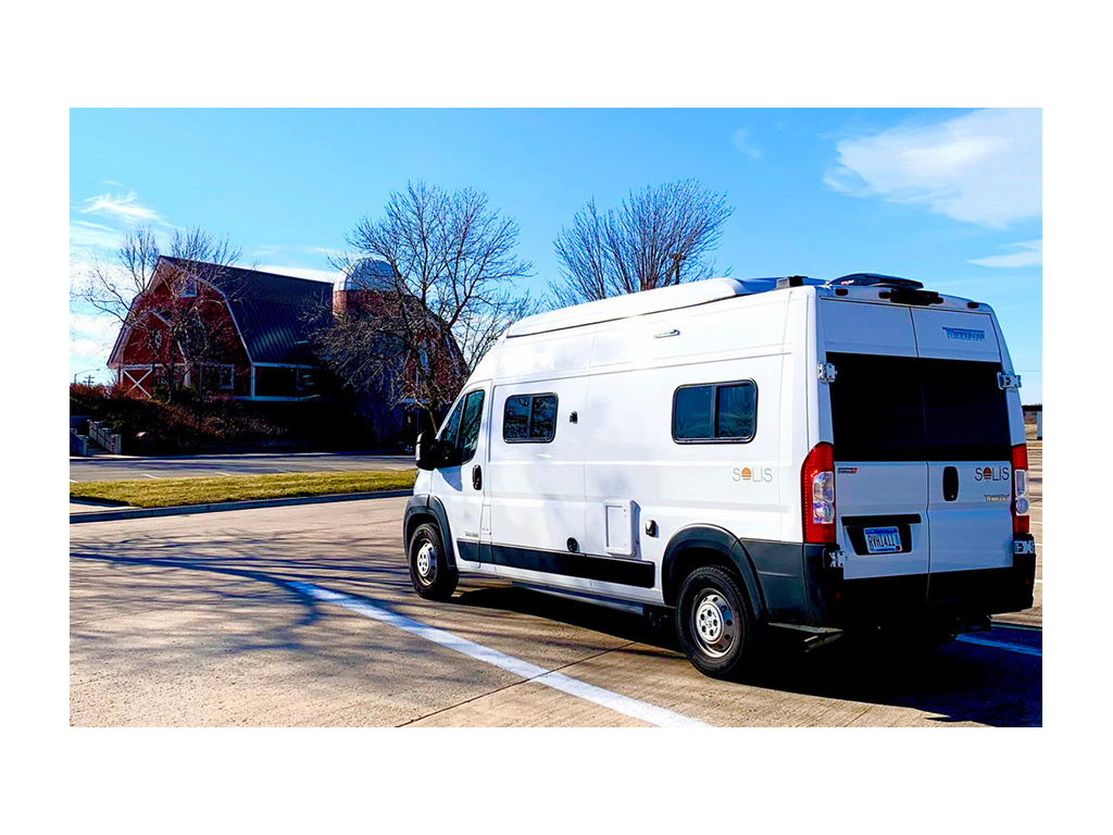 Winnebago Solis parked in parking lot across the street from a red barn