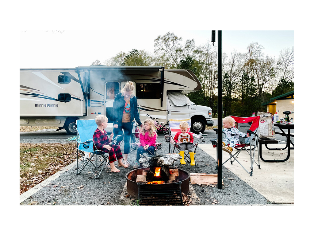 Tera and kids sitting around a fire with Minnie Winnie in background.
