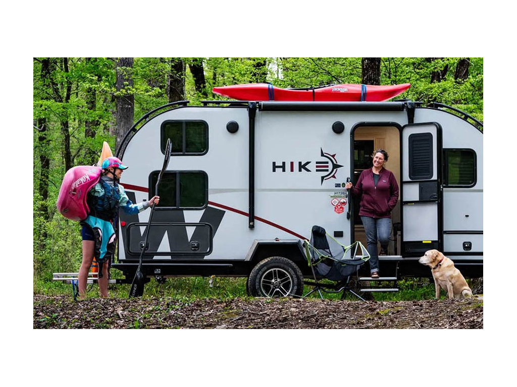 Kathy Holcombe standing in doorway of Winnebago Hike smiling at Abby Holcombe who is carrying kayak and paddle. Their yellow lab, Tucker, is sitting nearby.